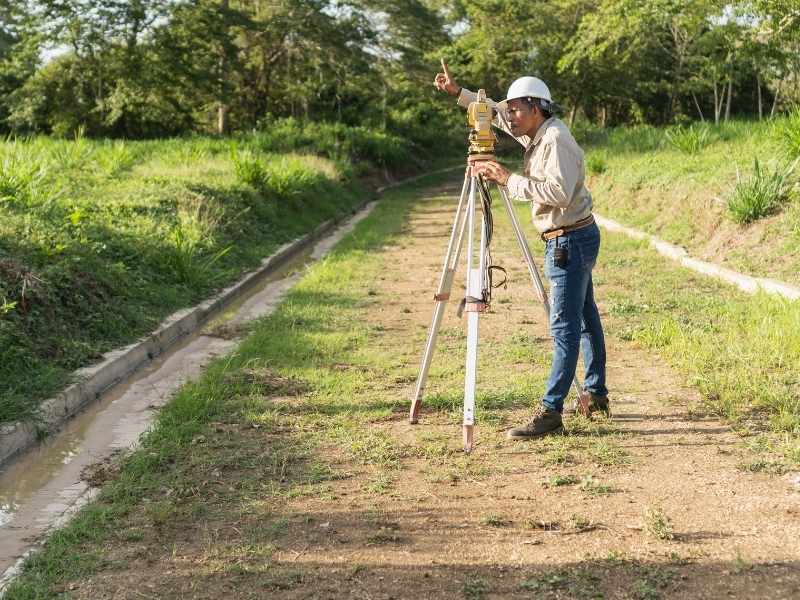 Land surveyor using a total station to measure and map property boundaries on a field site during a land survey