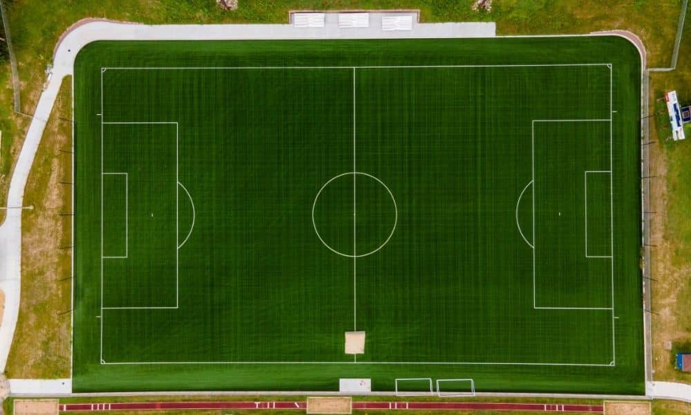 Aerial view of an athletic field showing the playing surface, running track, surrounding walkways, and landscaped areas relevant to a topographic survey